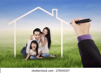 Cheerful Asian Family Laughing Together On The Meadow Under A Dream House