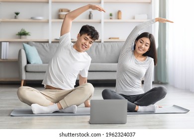 Cheerful Asian Family Practicing Yoga At Home, Stretching On Fitness Mat, Looking At Laptop Screen, Having Online Class, Living Room Interior, Copy Space. Sporty Black Couple Exercising Together