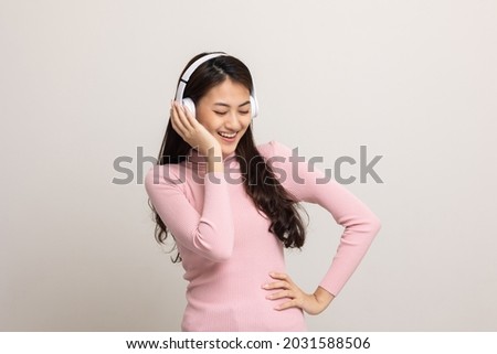 Cheerful asian female teenager listen to the music with white headphone on isolated. Beautiful young woman in pink shirt hand touch a wireless headphone having fun with the music in  room.