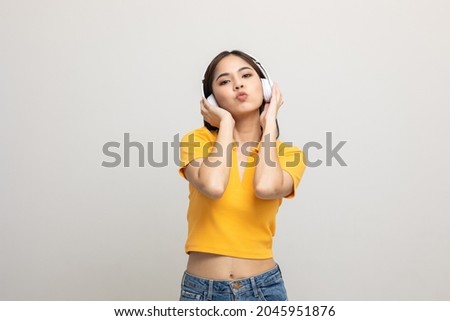Cheerful asian female teenager listen to the music with white headphone on isolated. Beautiful young woman in yellow shirt hand touch a wireless headphone having fun with the music in  room.