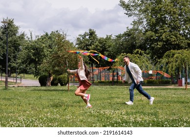 Cheerful Asian Girl Playing With Flying Kite Near Dad In Park