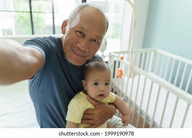 Cheerful Asian Grandparent And Little Cute Baby Boy Smiling Taking Selfie Photos With Smartphone At Home. Happy Different Generations Family Of Senior Man And Grandchild.