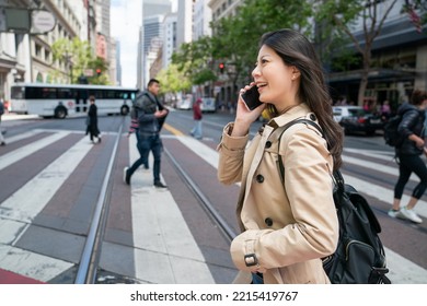 cheerful asian Korean businesswoman walking and talking on the cellphone while crossing road in the breeze in urban area of san Francisco in California usa - Powered by Shutterstock