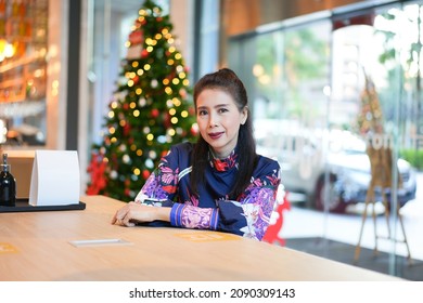Cheerful Asian Lady In Beautiful Dress Sitting In Coffee Shop And A Bar,Christmas Tree.