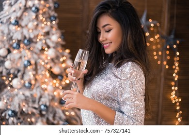 Cheerful Asian Lady In Beautiful Dress With A Glass Of Champagne. Sexy Smiling. Christmas Party. Christmas Eve. X-mas, Winter Holidays And People Concept