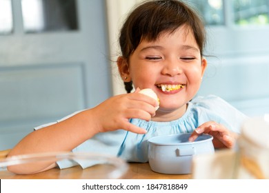 Cheerful Asian Little Girl Enjoy Eating Boiled Egg In Kitchen.