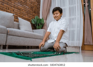 Cheerful Asian Muslim Kid Wearing Koko Shirt Dress Praying Alone On The Prayer Mat