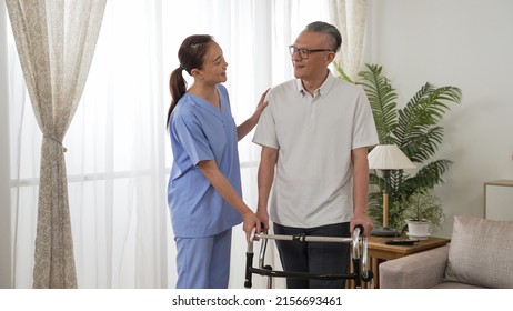 Cheerful Asian Older Man Under Recovery Process Is Talking Happily With Female Nursing Aide By Window In A Bright Home Interior. He Stands With The Support Of Walker