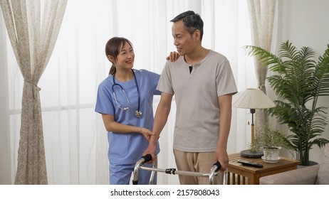 Cheerful Asian Older Man Under Recovery Process Is Talking Happily With Female Nursing Aide By Window In A Bright Home Interior. He Stands With The Support Of Walker