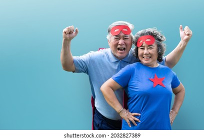 Cheerful Asian Senior couple wearing superhero costume standing on blue isolated background.