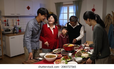 cheerful asian senior mother in red clothes talking to her son while daughter in law preparing hot pot with chopsticks at dining table. getting ready for lunar new year reunion dinner