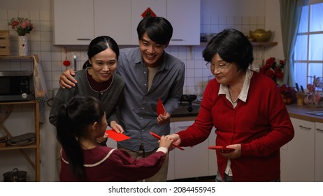 Cheerful Asian Senior Mother In Red Clothes Giving Red Envelopes To Surprised Adult Son, Daughter In Law And Granddaughter With Hand Gestures After Dinner On Chinese New Year's Eve