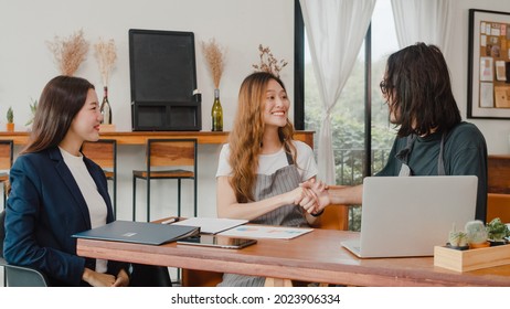 Cheerful Asian Small Business Owners Couple Meeting With Consultant Talking About Business Plan And Finance In Cafe. Young Japanese Agent Consider Signing Contract Insurance Together At Restaurant.