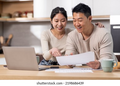 Cheerful asian spouses paying bills on Internet from home, sitting together at kitchen table, holding letters and papers, using computer and smiling, enjoying easy e-banking, copy space - Powered by Shutterstock