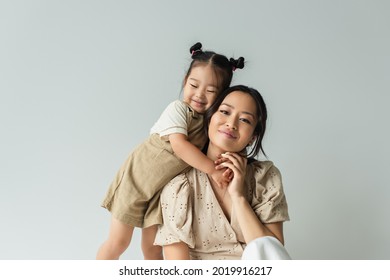fröhliche asiatische Kleinkind-Tochter, die glückliche Mutter einzeln auf Grau umarmt