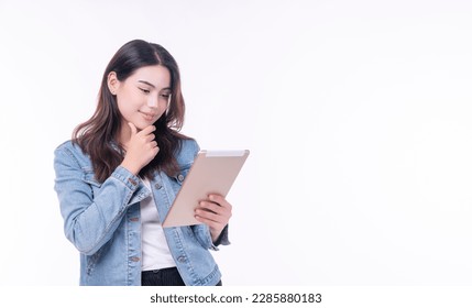 Cheerful asian woman denim jacket holding tablet thinking creative idea standing over isolated white background. Student young girl holding hand under chin education online tablet.Lifestyle technology - Powered by Shutterstock