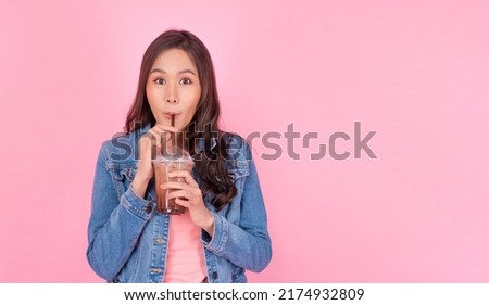 Cheerful asian woman drink ice cocoa with straw thirsty refreshment  looking camera on pink background. Portrait excited girl holding ice beverage in cup plastic use straw drinking relax over isolated