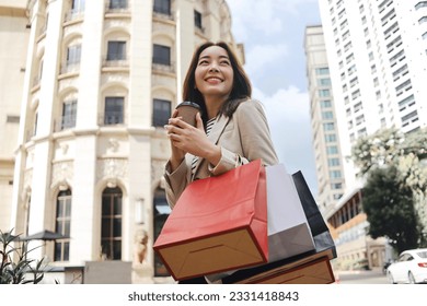 Cheerful Asian woman holding shopping bags.Beautiful Asian woman in casual style shopping in the city. - Powered by Shutterstock