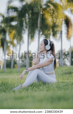 Cheerful Asian woman listening to music on smartphone Relax after exercising in the park.