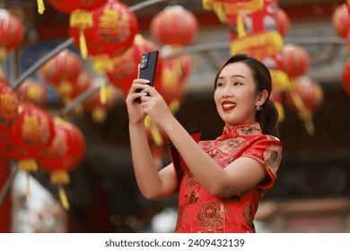 A cheerful  asian woman wearing red qipao cheongsam dress using a smartphone at the shrine, Chinese New Year