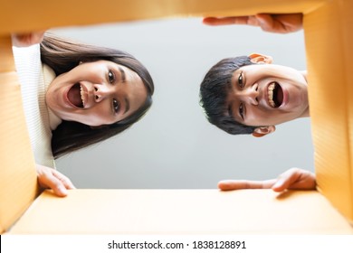 Cheerful Asian Young Couple Opening Cardboard Box Or Parcel And Looking Inside