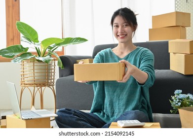 A Cheerful Asian Young Female Small Business Entrepreneur Holding A Cardboard Box Or Small Parcel Box. SME Online Retail Business.