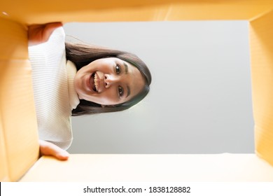 Cheerful Asian Young Woman Opening Cardboard Box Or Parcel And Looking Inside