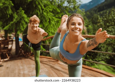 Cheerful athletic couple in sportswear doing exercises during yoga practice on wooden terrace in mountains - Powered by Shutterstock