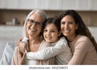 Cheerful attractive grandmother, mother and granddaughter kid hugging with love, enjoying bonding, close relationship, family leisure, looking at camera with perfect toothy smiles - Powered by Shutterstock