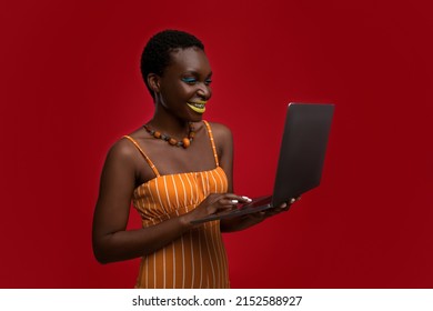 Cheerful Attractive Millennial Black Woman Using Brand New Computer On Red Studio Background, Stylish Young Lady Surfing On Internet, Looking For Job Online, Wearing Bright Look, Copy Space