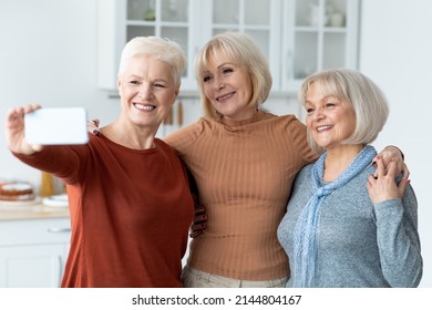 Cheerful attractive senior ladies in casual outfits taking selfie together, using smartphone. Three female friends spending time together at kitchen, cooking or drinking tea, closeup portrait - Powered by Shutterstock