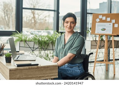 cheerful attractive woman with disability in her wheelchair looking at camera during work in office - Powered by Shutterstock