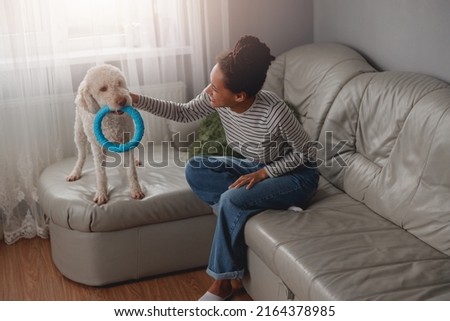 Cheerful attractive young female playing with dog sitting on couch at home