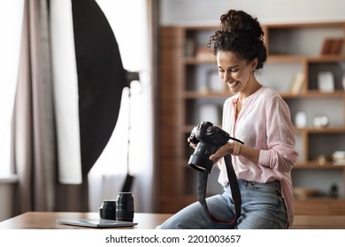 Cheerful attractive young lady in casual outfit photographer sitting on table at studio or office, holding professional camera, checking photos and smiling, copy space. Jobs and occupations concept - Powered by Shutterstock