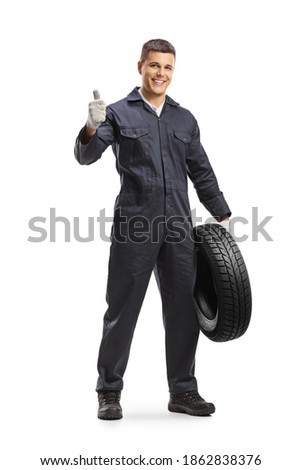 Cheerful auto mechanic worker holding a car tire and showing thumbs up isolated on white background