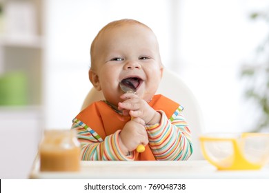 Cheerful baby child eats food itself with spoon. Portrait of happy kid boy in high chair. - Shutterstock ID 769048738