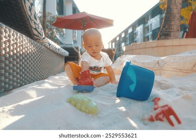 A cheerful baby enjoys playtime with colorful toys on warm beach sand under the sun - Powered by Shutterstock