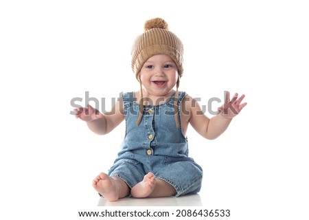 Cheerful baby sitting on a isolated floor with a wooled hat 