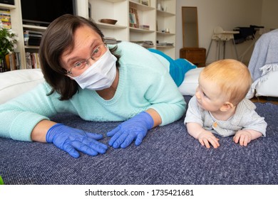 Cheerful Babysitter In Mask And Gloves Training Baby To Crawl, Playing With Child On Floor At Home. Closeup Shot. Quarantine Or Babysitting Concept