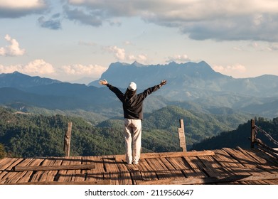 Cheerful back view of asian woman standing arms raised on wooden balcony with mountain peak in countryside at Chiang Mai, Thailand - Powered by Shutterstock