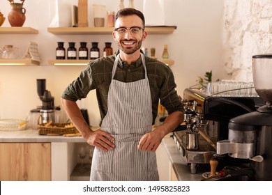 Cheerful barista. Cheerful dark-haired bearded barista smiling while welcoming guests