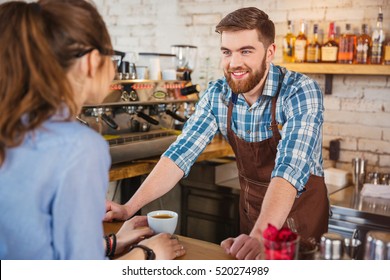 Cheerful bearded barista talking with young woman in coffee shop