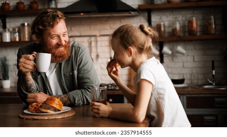 Cheerful bearded father holding coffee while daughter eating donut during breakfast in kitchen  - Powered by Shutterstock