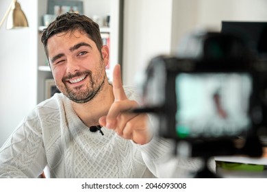 Cheerful Bearded Man In Sweater With Clip On Microphone Broadcasting Personal Show In Front Of Camera And Pointing With Finger Up In Excitement