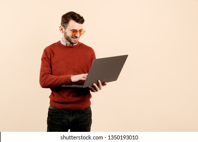 Cheerful bearded young man in casual outfit use notebook or computer over beige background. - Shutterstock ID 1350193010