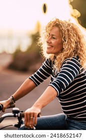 Cheerful beauiful blonde curly caucasian woman smile and enjoy the ride on a bike in outdoor leisure activity in the city - free and joyful active people on the street having fun