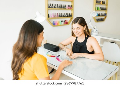 Cheerful beautician talking to a customer about the gel nail colors before doing a manicure service in the nail salon - Powered by Shutterstock