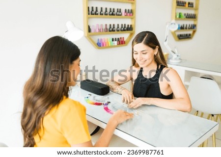 Cheerful beautician talking to a customer about the gel nail colors before doing a manicure service in the nail salon