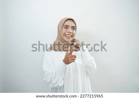 Cheerful beautiful Asian woman in casual shirt and hijab pointin