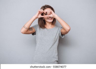 Cheerful beautiful girl making heart by hands isolated on a gray background